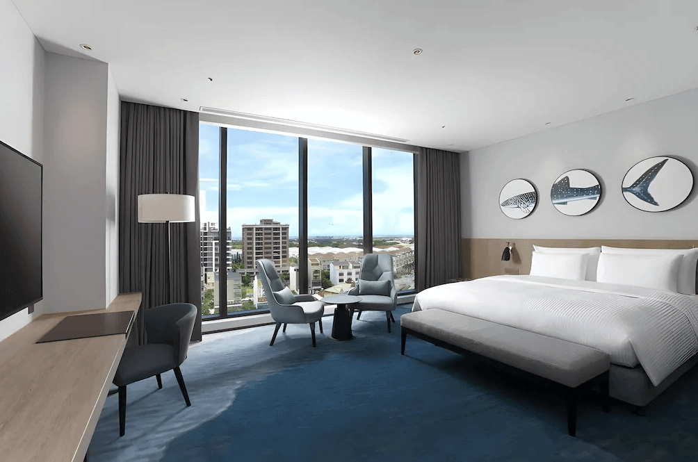 【桃園機場住宿】“Xpark住宿”COZZI Blu 和逸飯店 桃園館的現代雙人客房，大片落地窗望向桃園市區景致，房內設有一張大床、沙發座椅與簡約風書桌，空間明亮寬敞。