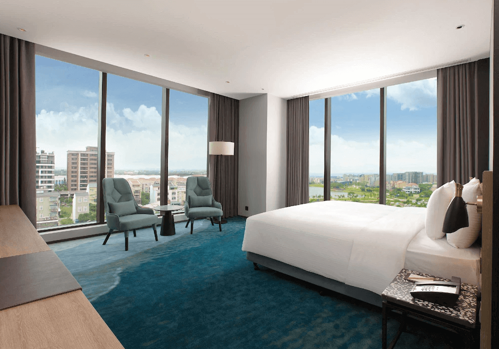 【桃園機場住宿】“Xpark住宿”COZZI Blu 和逸飯店 桃園館的轉角客房，擁有兩面環景落地窗，房內配有舒適雙椅與圓桌，視野遼闊可俯瞰桃園高樓與湖景。