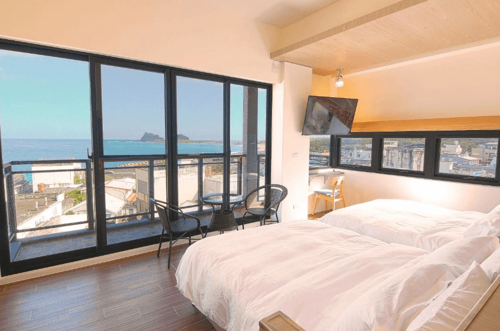 【台東成功住宿】台東「三仙台喜比民宿」海景房內景，房內有兩張舒適的大床，大片玻璃窗提供絕佳的海景視野，窗外即是湛藍的大海與三仙台著名的島嶼地標，明亮舒適。