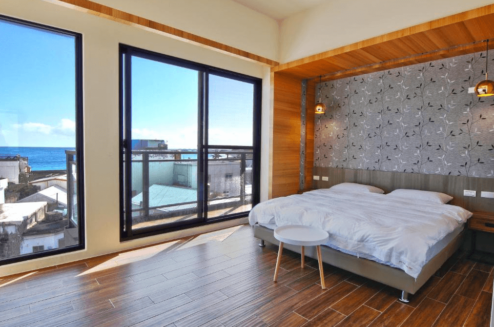 【台東成功住宿】台東「三仙台喜比民宿」雙人海景房內景，房間設有一張寬敞的雙人床，房內裝潢簡約雅致，大片落地窗及陽台可欣賞遼闊海景，充滿放鬆與療癒的氛圍。