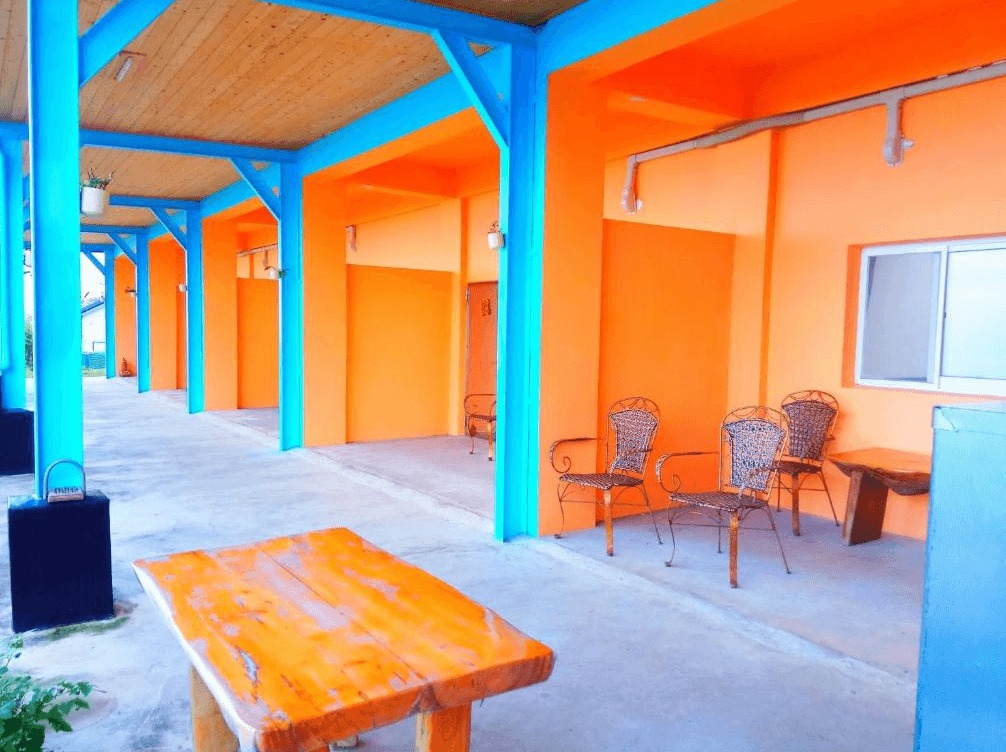 【台東成功住宿】台東「三仙台小月光民宿」建築外觀走鮮明色調設計，橘色牆面搭配藍色樑柱，門前備有戶外座椅與木桌，環境親切可愛，充滿度假氛圍。
