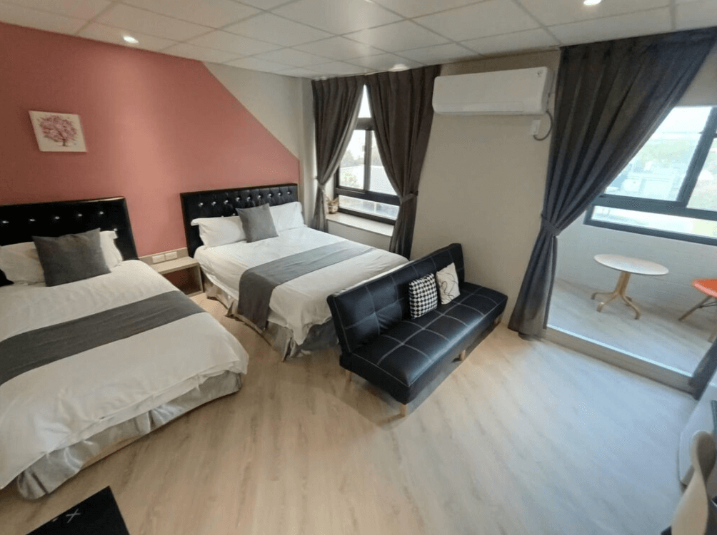 【布袋住宿】光影民宿景觀四人房，配置兩張雙人床與一張黑色沙發床，牆面以粉紅色斜角設計增添視覺層次，三面開窗採光良好，另設有簡約圓桌與雙人沙發區。