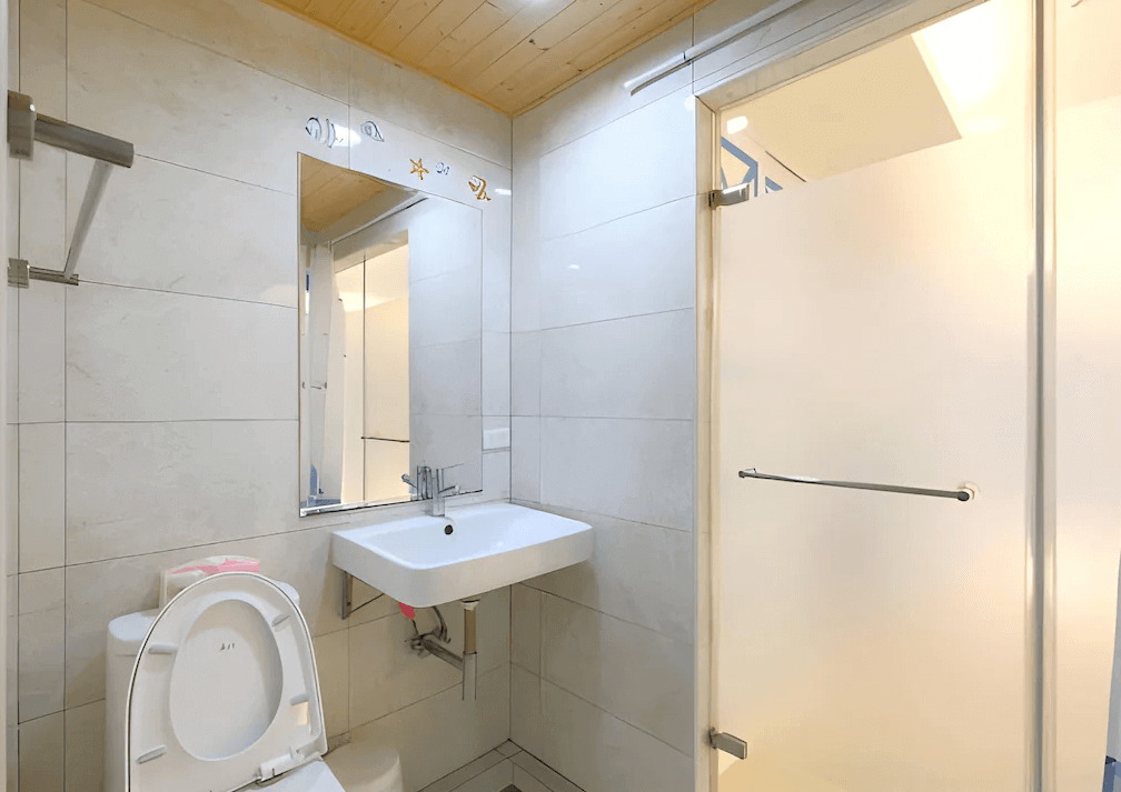 【高雄寵物友善住宿】八五亞太旅店的衛浴採用白色磁磚與木紋天花設計，設有獨立馬桶、洗手台與乾濕分離淋浴間，空間明亮清潔，提供基本盥洗設施，實用又舒適。