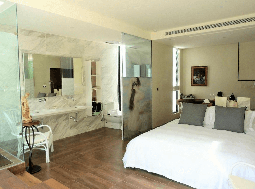 【苗栗包棟民宿】八角隱士莊園，客房與浴室以玻璃隔間設計，採用大理石與木地板質材融合，整體風格高雅，設有雙人床、古典風擺設與泡澡浴缸，呈現現代與藝術兼具的住宿空間。