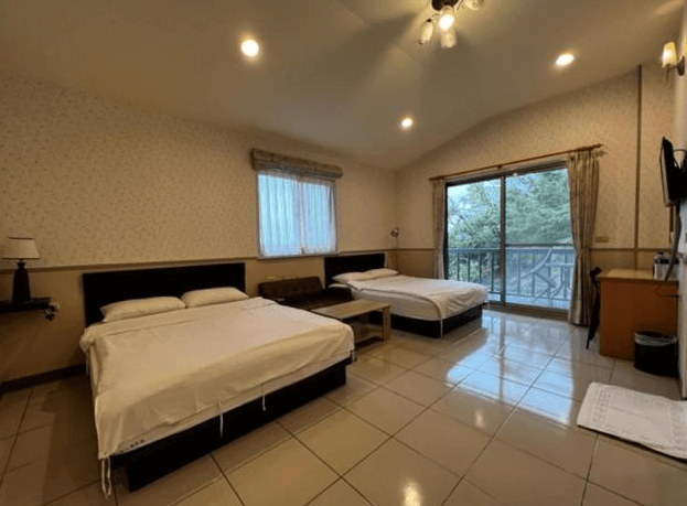 【東河住宿】南八里民宿四人家庭房，配置兩張雙人床與沙發茶几，室內鋪設淺色磁磚，挑高斜屋頂與陽台設計增添空間感，窗外可見山林景致，適合親子與好友同住。