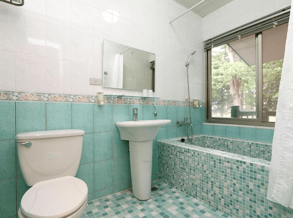 【東河住宿】南八里民宿浴室，採用綠白拼接磁磚設計，設有浴缸、馬桶與洗手台，對外窗可望見自然綠意，空間明亮清潔，融合復古與實用風格。