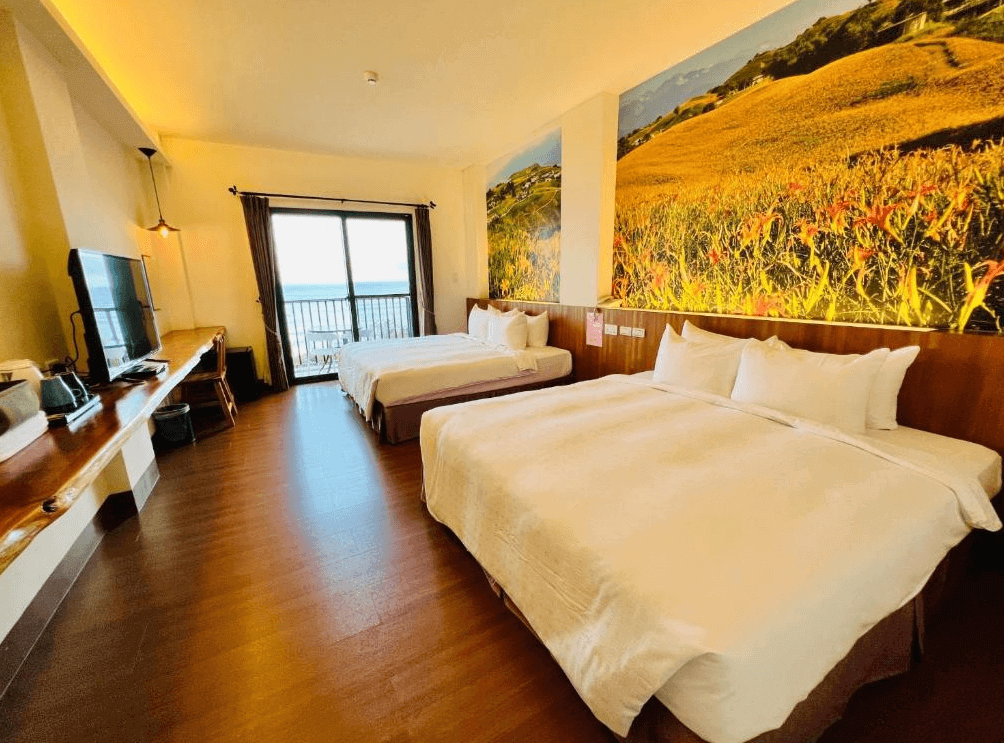 【台東成功住宿】台東「嵐海民宿」四人海景房內景，房間空間寬敞舒適，牆上有大型自然景觀壁畫，房內設置兩張柔軟的雙人床及實木書桌，落地窗戶可直接欣賞美麗的海景。
