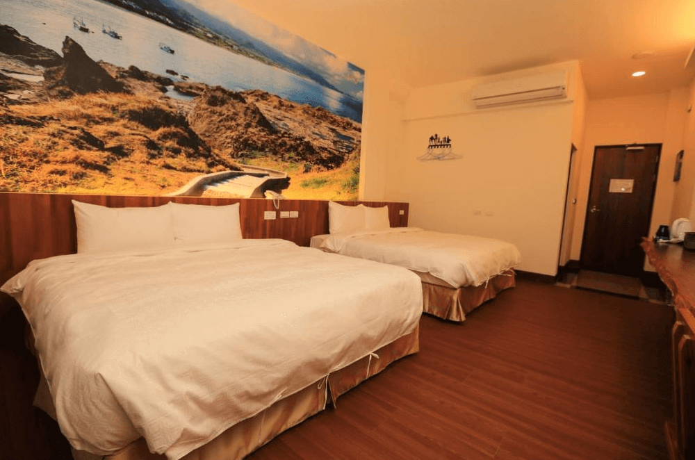 【台東成功住宿】台東「嵐海民宿」四人房內景，房內設有兩張舒適的雙人床，牆面裝飾以台東特色自然景觀為主題，搭配溫暖的燈光，提供溫馨舒適的住宿氛圍。