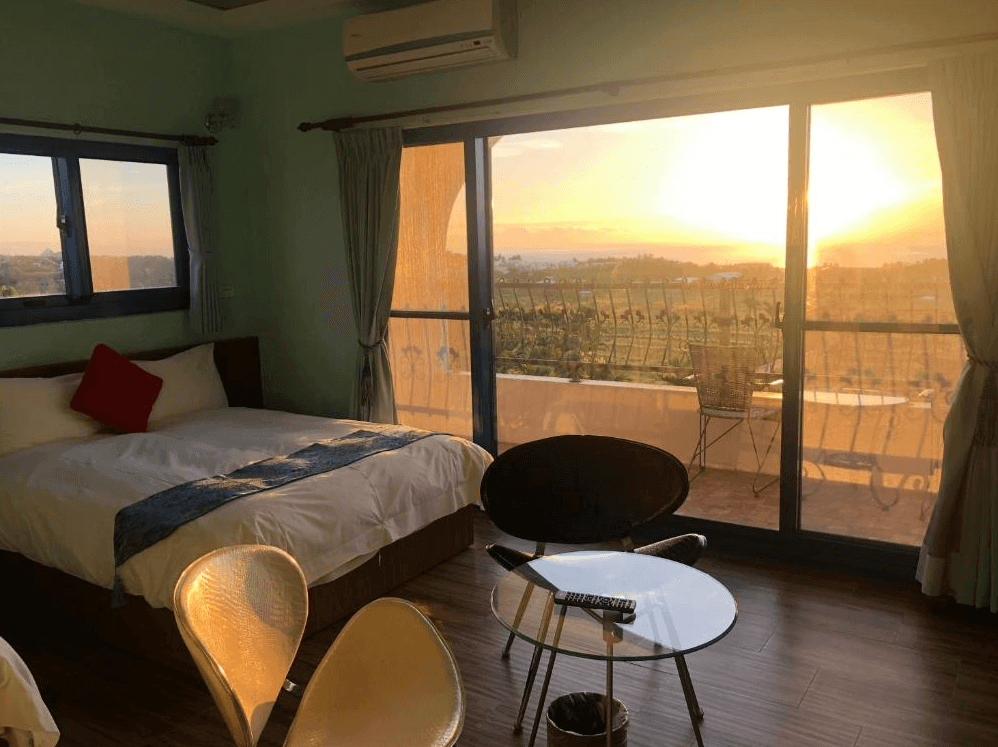 【台東成功住宿】台東「幸福小築民宿」雙人房傍晚景色，房間設有大片落地窗與陽台，可直接觀賞夕陽西下的田園美景，陽光灑落在室內，營造溫暖又浪漫的氛圍。