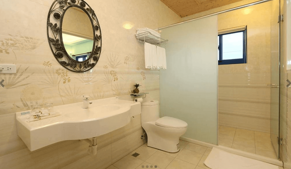 【台東成功住宿】台東「幸福小築民宿」衛浴空間，設有乾濕分離淋浴間、簡潔的洗手台與優雅圓形鏡面，牆面為溫和米色花草紋路磁磚，整體清潔明亮。