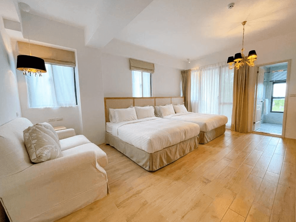 【台東成功住宿】台東海景民宿「奧麗雅安莊園」的四人房內景，房間寬敞明亮，設有兩張舒適雙人床，搭配柔和的燈光、簡約雅致的沙發，以及可觀賞窗外景致的大型窗戶，適合家庭或朋友同遊。