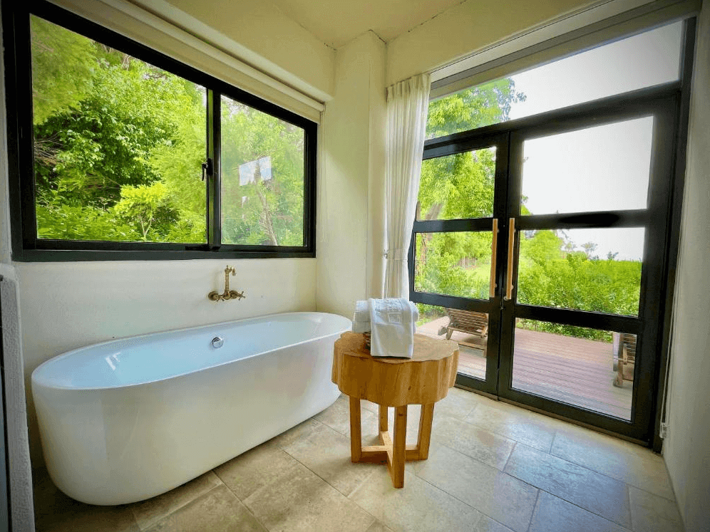 【台東成功住宿】台東海景民宿「奧麗雅安莊園」的浴室空間設計，設有大型浴缸，兩面皆為大片玻璃窗戶，窗外綠意盎然，可邊泡澡邊欣賞戶外的自然景觀，提供舒適放鬆的沐浴體驗。