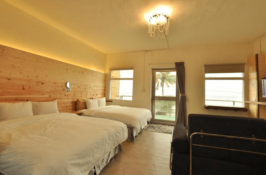 【長濱住宿】台東跑者之家民宿四人房，木質牆面與暖色燈光營造溫馨氛圍，設有兩張大床、大片窗戶可見棕櫚樹與戶外綠意景觀。