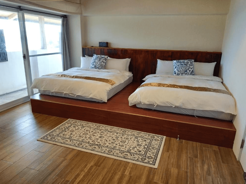 【台東成功住宿】台東「馬可樓民宿」雙人大床房內景，採用溫暖木質地板，兩張舒適雙人床設置於木製平台上，房內設有落地窗可通往陽台，明亮寬敞，適合家庭或好友住宿。