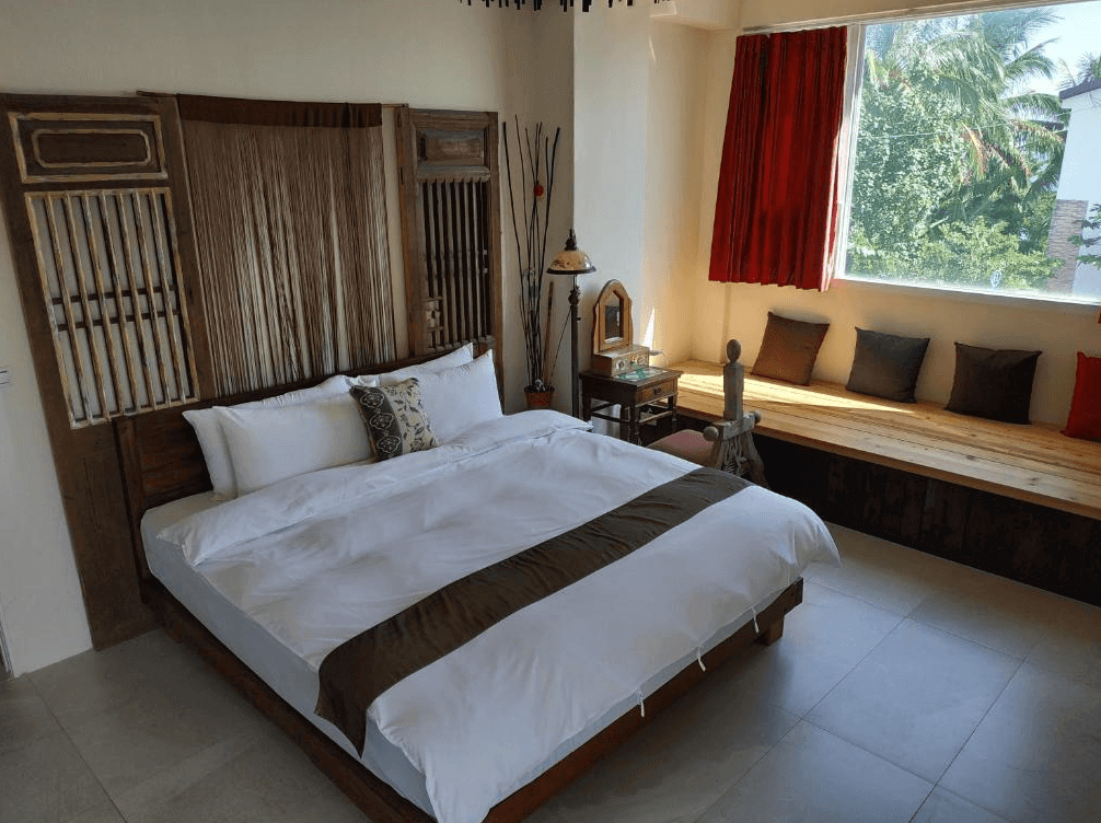 【台東成功住宿】台東「馬可樓民宿」雙人房內景，房間設計充滿異國風情，床頭以特色木質裝飾，窗邊設有寬大的木製臥榻，並配置柔軟靠枕，可欣賞窗外綠意盎然的自然景色，整體空間典雅舒適。