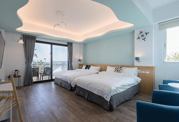 【東河住宿】吉院子民宿家庭四人房，設有兩張雙人床，天花板造型流線富有設計感，牆面為柔和的藍綠色，房內配備圓桌、休憩沙發椅與陽台座椅，適合親子或好友入住。