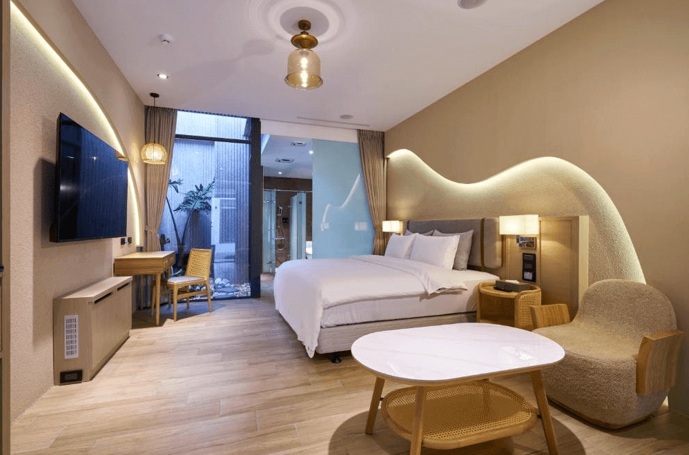 【桃園機場住宿】“Xpark住宿”和陽行館的自然風格雙人房，牆面以波浪燈帶設計營造柔和氣氛，房內設有木質傢俱、書桌與落地窗，望向戶外小庭景觀。