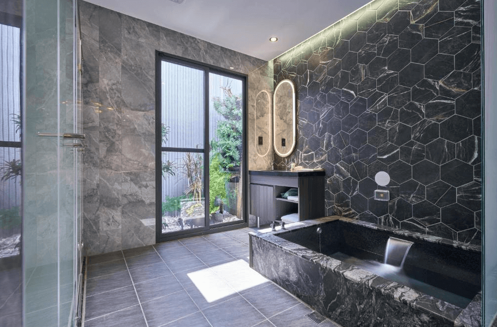 【桃園機場住宿】“Xpark住宿”和陽行館的豪華湯屋空間，整體以深色大理石與六角磚牆面打造，內含獨立浴池與雙面鏡洗手台，窗邊可見綠意造景，營造沉靜療癒氛圍。