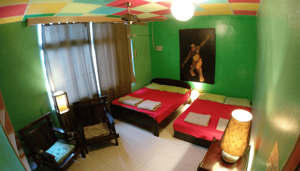 【東河住宿】哇軋力共四人房，綠色牆面與繽紛天花板營造出活潑氣氛，房內設有兩張雙人床，搭配木椅與原民風裝飾畫作，整體風格融合原住民與熱帶元素，適合好友同住。