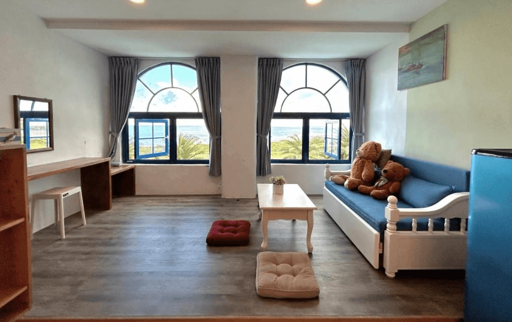 【豐濱住宿】太平洋渡假村的客廳空間擁有拱形窗框設計，可遠眺椰林與蔚藍海岸，室內配有書桌、沙發床與大型泰迪熊，營造出溫馨放鬆的氛圍，適合親子與家庭入住。