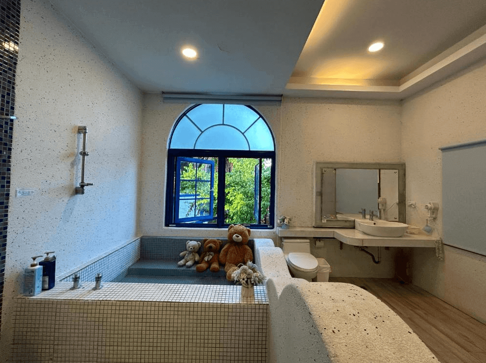 【豐濱住宿】太平洋渡假村浴室內設有大型泡湯池，窗邊擺放多隻可愛泰迪熊，牆面以柔和色調瓷磚鋪設，搭配拱形窗景與自然光，營造出療癒又具童趣的衛浴空間。