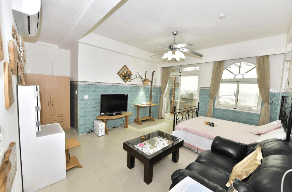 【台東成功住宿】台東「宜人海灣山海景民宿」海景雙人房內景，房內配置雙人床、沙發及電視，牆面為藍綠色瓷磚，窗外可欣賞海景與日落，整體風格溫馨又具有度假感。