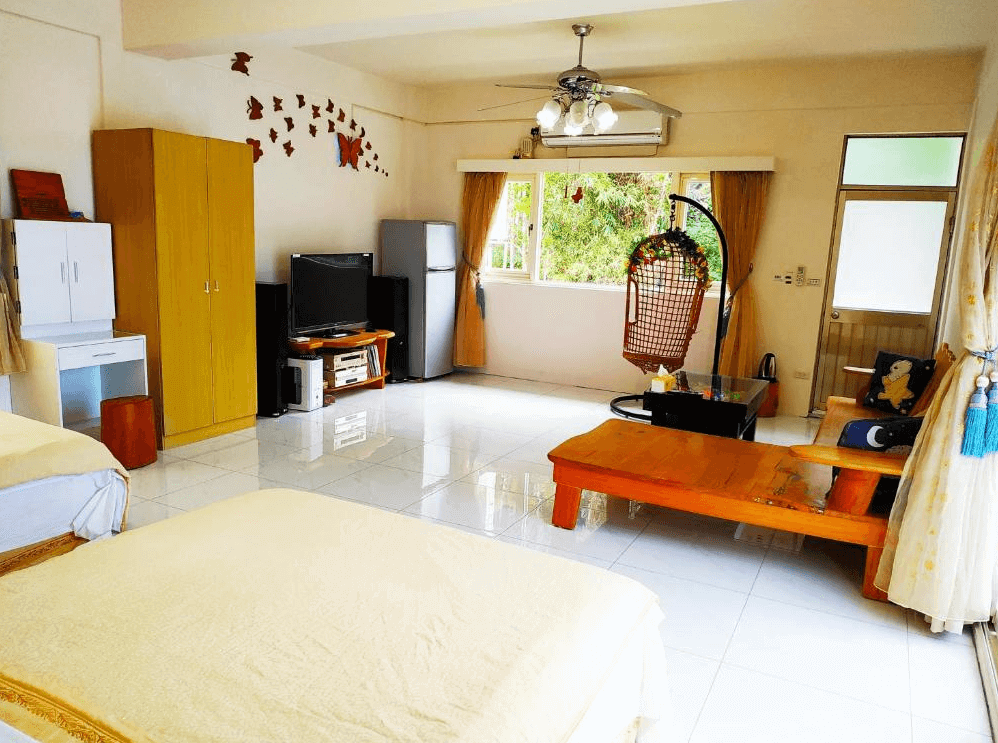 【台東成功住宿】台東「宜人海灣山海景民宿」四人房空間寬敞，內有兩張雙人床、木質桌椅及吊籃椅，落地窗外為翠綠山林景觀，室內採光充足，氛圍溫暖舒適。