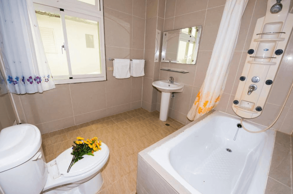 【台東成功住宿】台東「宜人海灣山海景民宿」浴室空間簡潔明亮，設有按摩淋浴系統及浴缸，窗邊擺有花束增添溫馨氣息，牆面為淺色瓷磚，乾淨整潔。