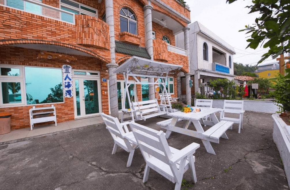 【台東成功住宿】台東「宜人海灣山海景民宿」建築外觀，紅磚建築風格融合歐式與台式元素，門前設有白色戶外座椅與鞦韆，營造出悠閒愜意的住宿環境。
