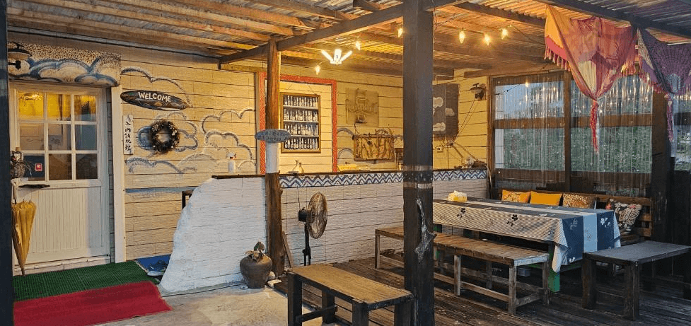 【長濱住宿】小阿姨野花戶外交誼空間，牆面手繪雲朵與船錨裝飾，設有長桌與木椅，燈光溫暖柔和，整體洋溢手作與藝術氣息。