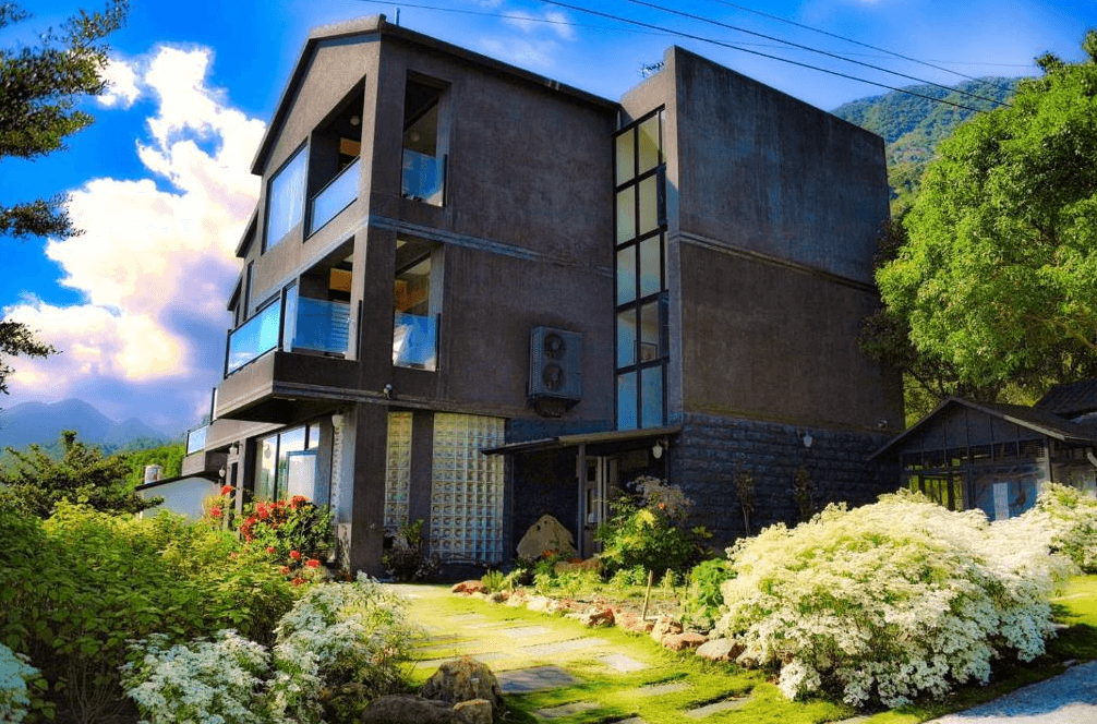 【台東成功住宿】台東「小馬日光涵館」建築外觀，為現代風格的三層樓建築，坐落於綠意盎然的庭園中，周圍種滿花草，遠處可見山巒景緻，環境清幽自然。