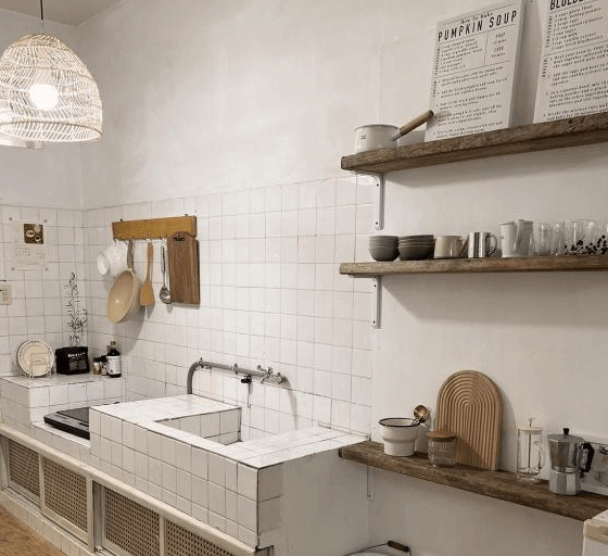 【玉井住宿】山蒔旁白的夜晚廚房實景照，空間保留白天的設計質感，溫暖黃光燈飾營造出柔和氛圍，開放式架上擺放整齊杯碗與茶具，整體簡約實用又富有生活品味。