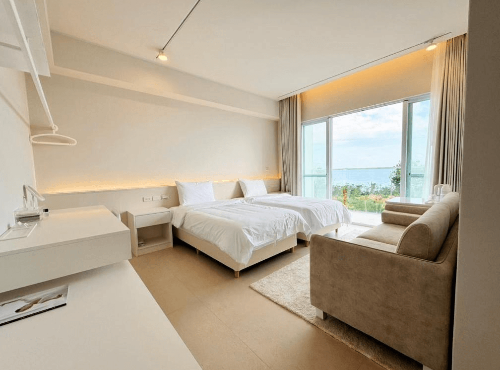 【東河住宿】川三白。秘境莊園雙床房，室內簡約現代設計，設有兩張單人床、沙發與大面積落地窗，坐擁太平洋海景與園區綠意，空間明亮開闊，非常適合放鬆休憩。