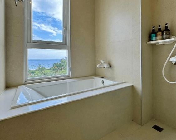 【東河住宿】川三白。秘境莊園浴室設有景觀浴缸，浴缸旁的窗戶可眺望外部山海景色，內部以米白色調鋪陳，簡潔乾淨，備有洗沐用品，為旅人帶來放鬆沐浴體驗。