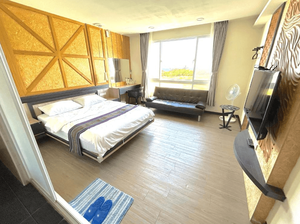 【台東成功住宿】台東「巴斯拉岸民宿」雙人房內景，房間設計簡約現代，搭配木質地板與特色幾何牆面，設有雙人床、沙發與大面窗景可望見戶外自然景色，整體明亮舒適。