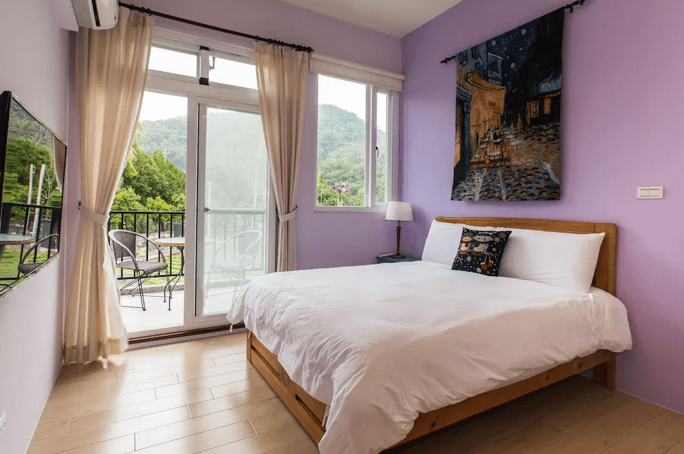 【關山住宿】弋式風莊園民宿的紫色景觀雙人房，房內布置簡約，設有舒適雙人床與窗邊畫作，大片窗戶外連接陽台，可欣賞綠意山景。