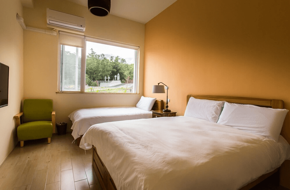 【關山住宿】弋式風莊園民宿的三人房型，配有一張雙人床與一張單人床，溫暖的橘黃色牆面搭配自然採光，整體氣氛溫馨放鬆。