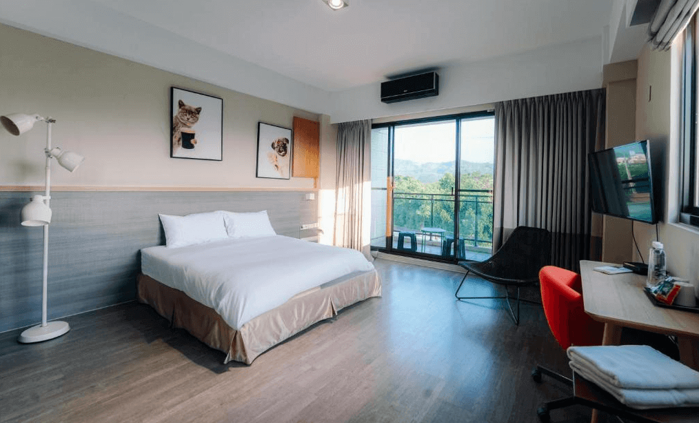 【玉井住宿】微風栩栩 & 晴意天空的雙人房型，簡約現代風格設計，配有一張大床，牆面裝飾有可愛貓狗掛畫，大片落地窗可遠眺綠意山景，房內設有電視、辦公桌與紅色椅子，空間寬敞明亮。