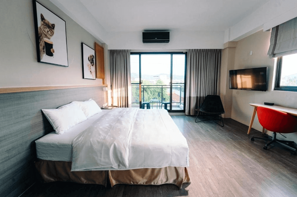 【玉井住宿】微風栩栩 & 晴意天空雙人房的正面視角，整體空間開闊，配置一張大床，搭配柔和木質地板與灰白色調牆面，窗外可欣賞遼闊山景，電視牆與簡約書桌設計讓旅客能放鬆或辦公皆宜。