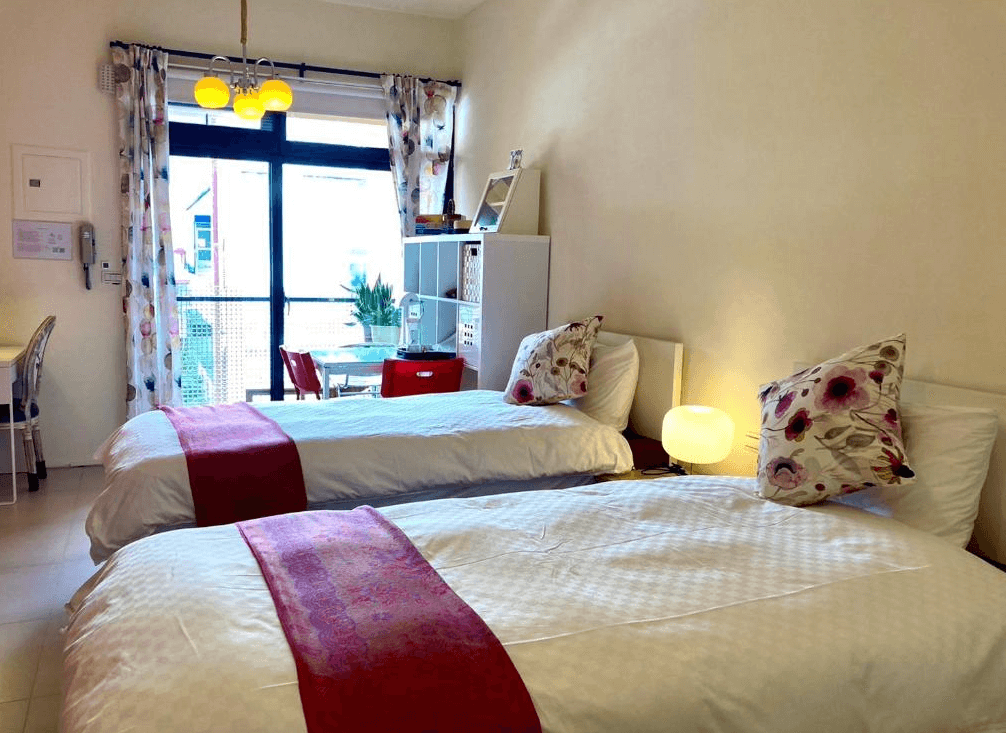 【東河住宿】心適都蘭雙床房另一角度，展示落地窗外陽台及閱讀空間，房內有紅色座椅與白色書櫃，整體擺設活潑明亮，適合長住與閱讀放鬆。