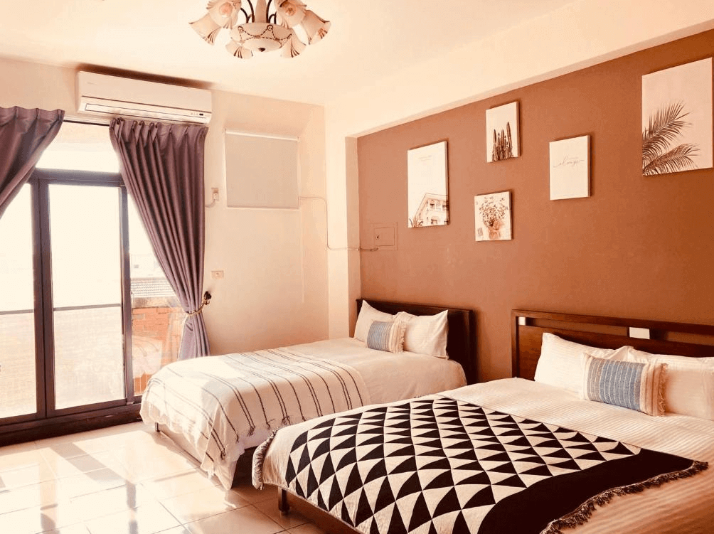 【玉井住宿】恩典之家民宿的溫馨四人房型，配置兩張雙人床，搭配柔和暖色系燈光與簡約掛畫，牆面採用奶茶色與白色跳色設計，空間整潔舒適，窗邊設有大片落地窗與紫色窗簾，採光良好。