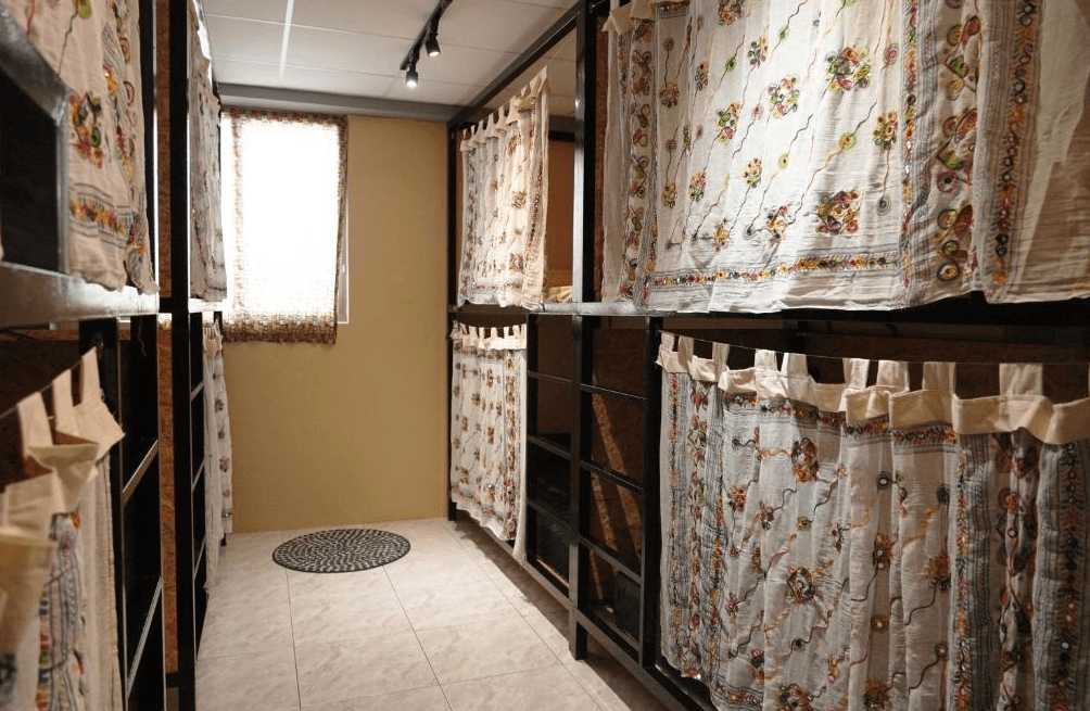 【東河住宿】旅行蟲背包客棧的上下舖宿舍房型，設有多張木製床位，並以花紋布簾提供隱私，昏黃燈光與整齊排列的床位營造溫暖與安靜的休息環境。