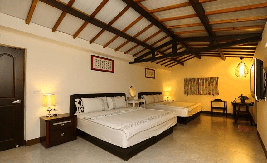 【關山住宿】春風小棧民宿的四人房型，木質橫梁天花板與暖黃色燈光營造溫馨氛圍，房內擺放兩張大床、化妝台與古典書桌，空間寬敞舒適。