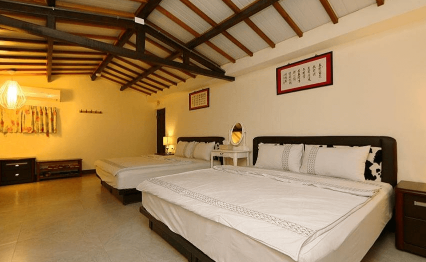 【關山住宿】春風小棧民宿融合中式元素的家庭房，兩張大床以書法字畫點綴牆面，搭配暖色調燈光與木作家具，營造典雅的住宿空間。