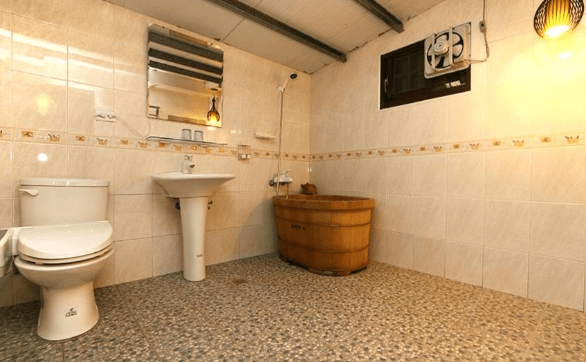 【關山住宿】春風小棧民宿的浴室空間，內有木桶浴缸、立式洗手台與馬桶，磁磚牆面與磨石子地板呈現懷舊風格，搭配昏黃燈光格外有味道。