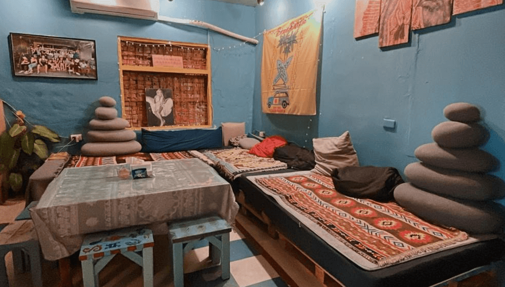 【東河住宿】晃輕鬆客棧咖啡館公共交誼區，以藍色牆面和舒適坐墊布置，牆上掛有特色布旗與藝術裝飾畫作，適合房客們休閒聊天交流，整體氛圍輕鬆自在。