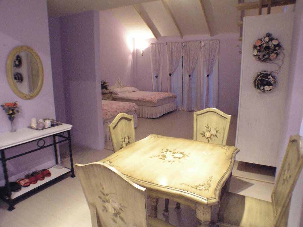 【苗栗包棟民宿】栗田庄民宿淡紫色牆面與碎花床罩營造溫馨感，搭配手繪鄉村風格木製餐桌椅與窗簾，空間寬敞，適合小家庭入住與用餐。