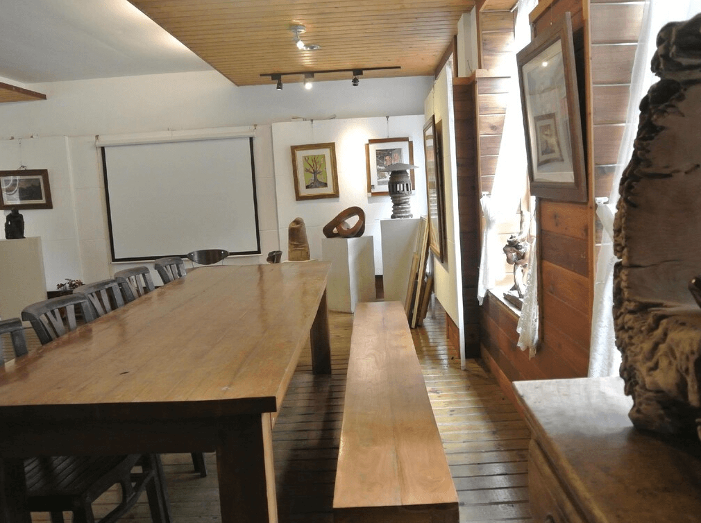 【苗栗包棟民宿】栗田庄民宿，結合木質與藝文元素的空間，設有長桌與投影布幕，牆上陳列多幅藝術作品與陶藝裝飾，適合作為展覽、閱讀或小型聚會空間。