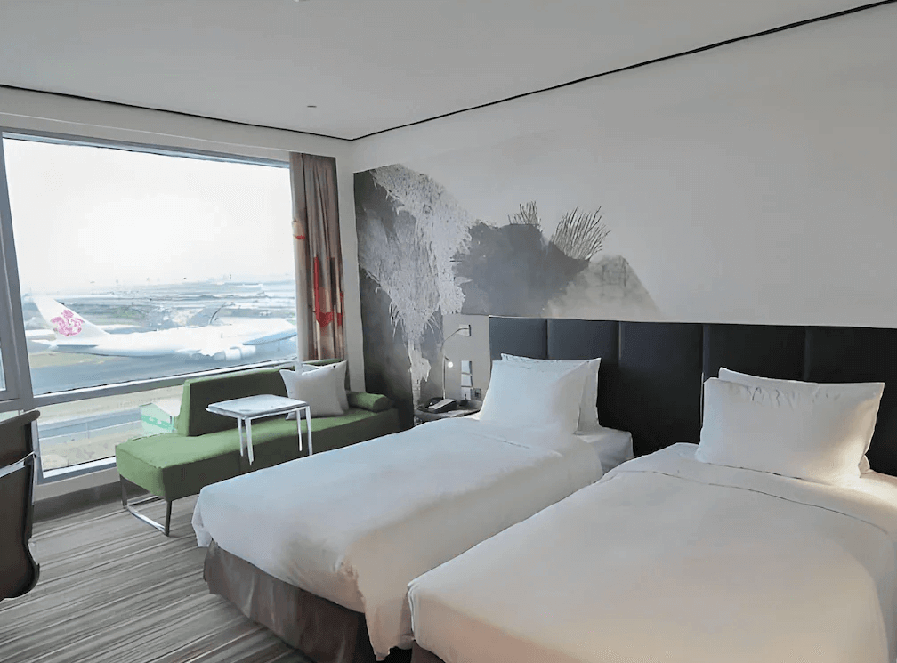【桃園機場住宿】桃園國際機場凱悅酒店的雙床房，大片玻璃窗外可清楚望見停機坪與華航飛機，房內設有綠色沙發與簡約書桌，充滿現代感與航空氛圍。