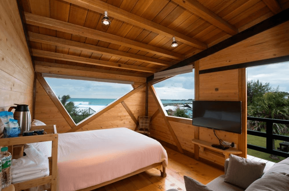 【台東成功住宿】台東「比西里岸營地渡假小木屋」雙人房內景，房間以木質元素打造，幾何造型窗框設計獨特，窗外即是湛藍海洋與綠意景觀，適合享受靜謐時光。